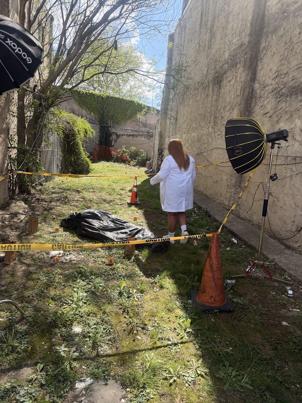 A staged concept shoot in an alley with caution tape, traffic cones, softbox lights, and a model in a white coat